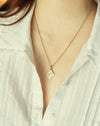 Gold necklace with a pendant worn by a person in a light-colored shirt.